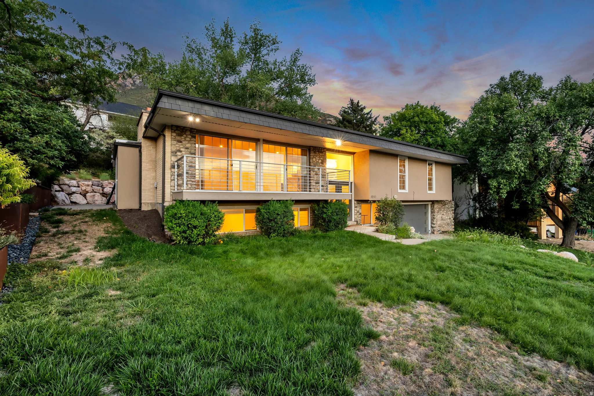 Contemporary exterior with stone facade, expansive windows, front balcony with cable railing, and integrated garage