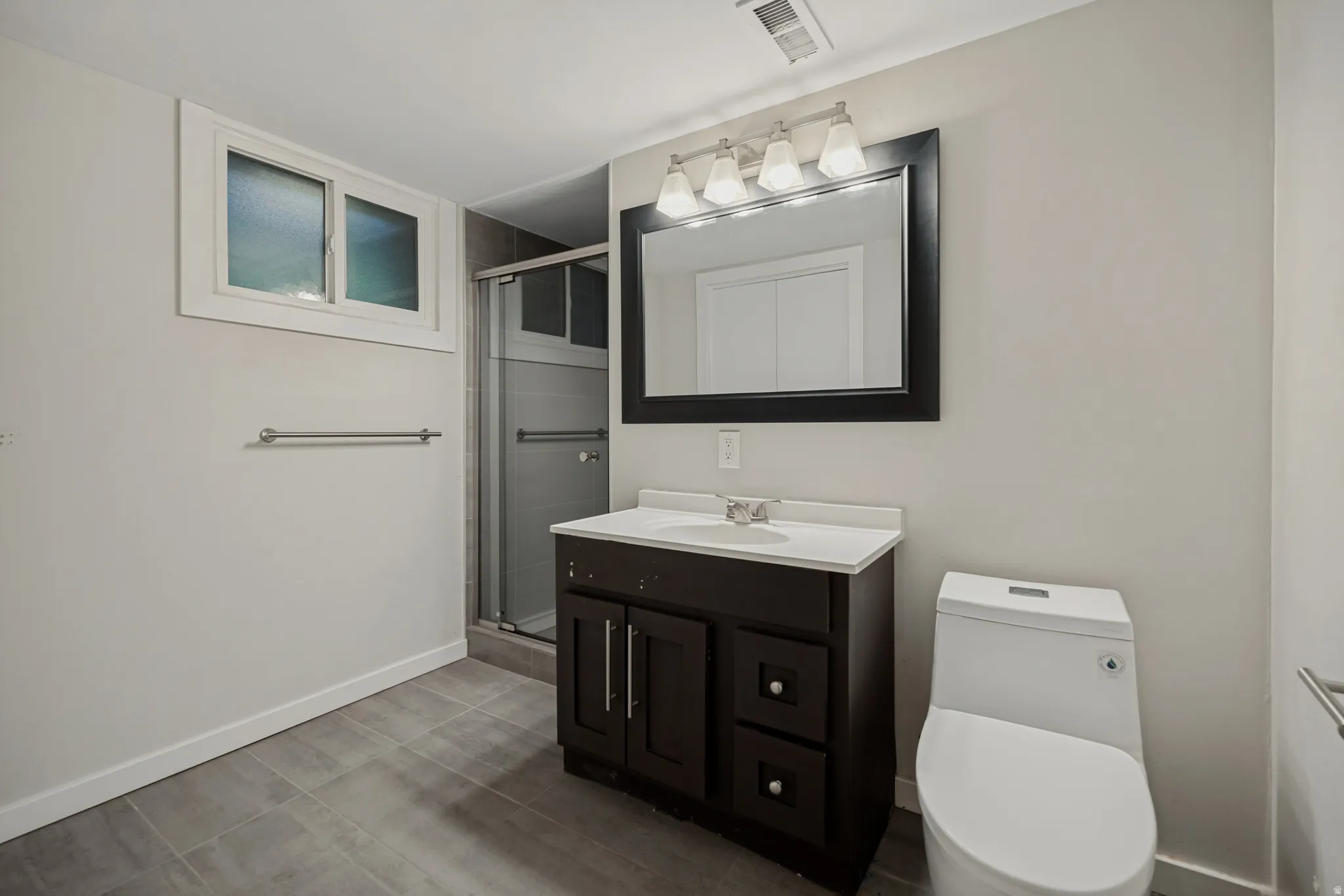 Bathroom featuring a dark wood-finish vanity, white countertop, framed mirror, and a glass-enclosed shower