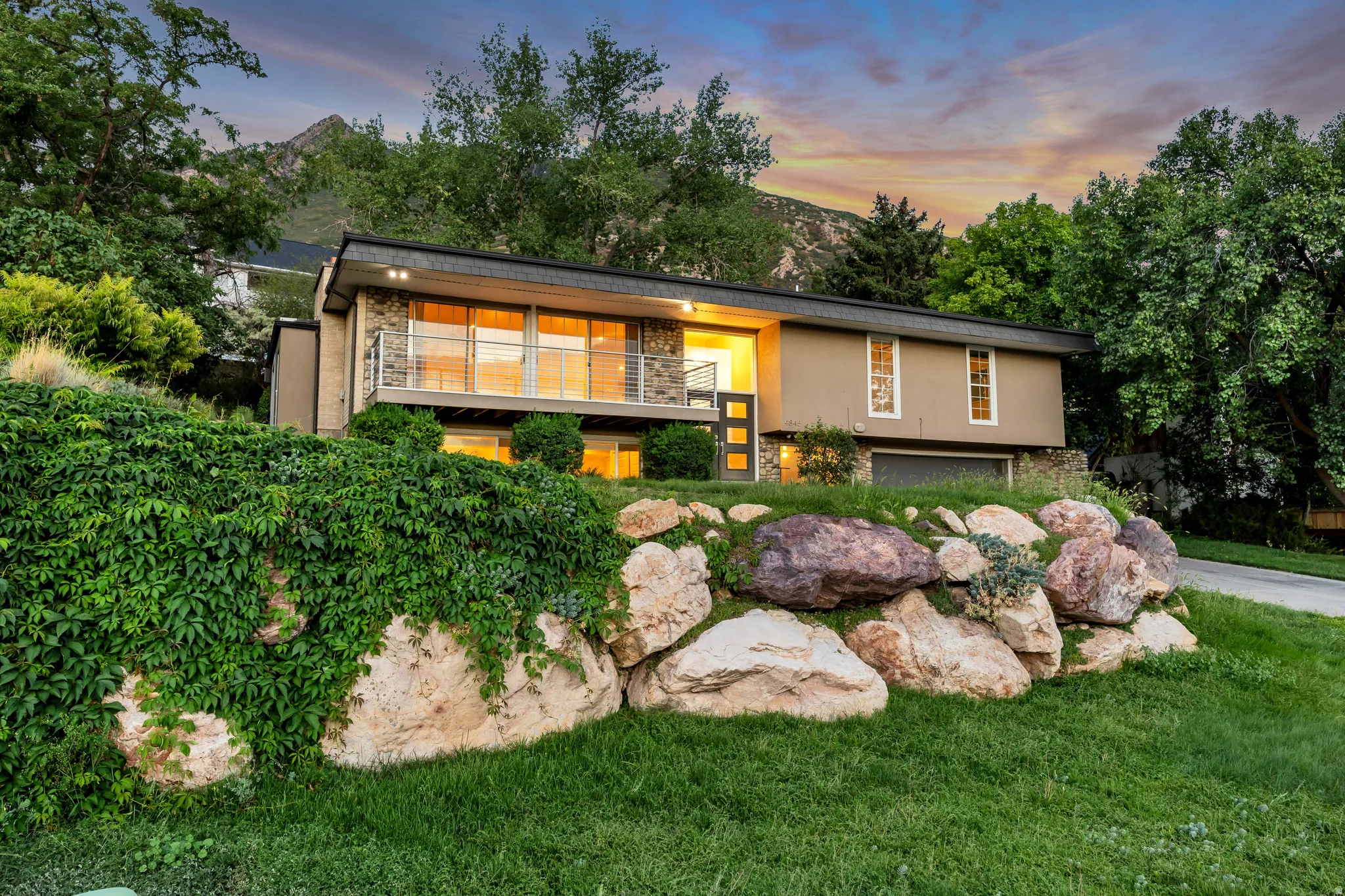 Modern exterior with a stone-finish facade, expansive windows, a full-width balcony with metal railings, a flat roofline, and an integrated garage