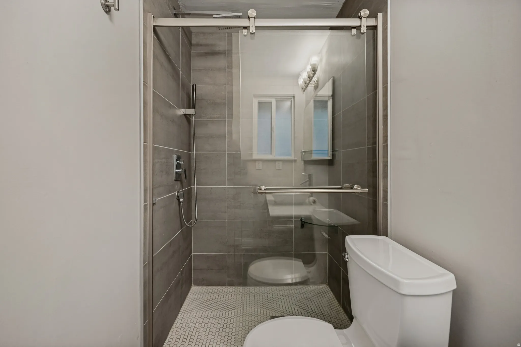 Walk-in shower with sliding glass door, large format tile surround, and mosaic tile flooring
