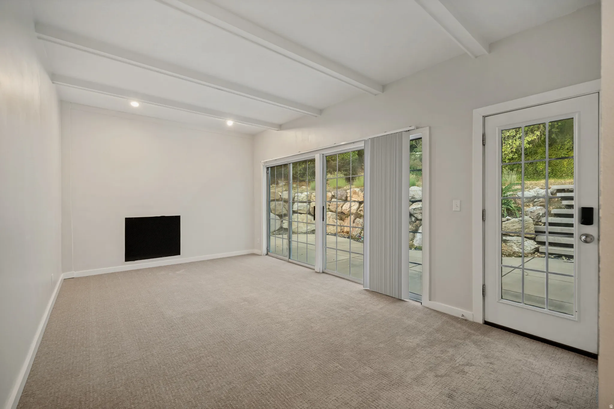 Recessed lighting with exposed ceiling beams, built-in fireplace, carpet flooring, sliding glass doors, and a glass-paneled entry door