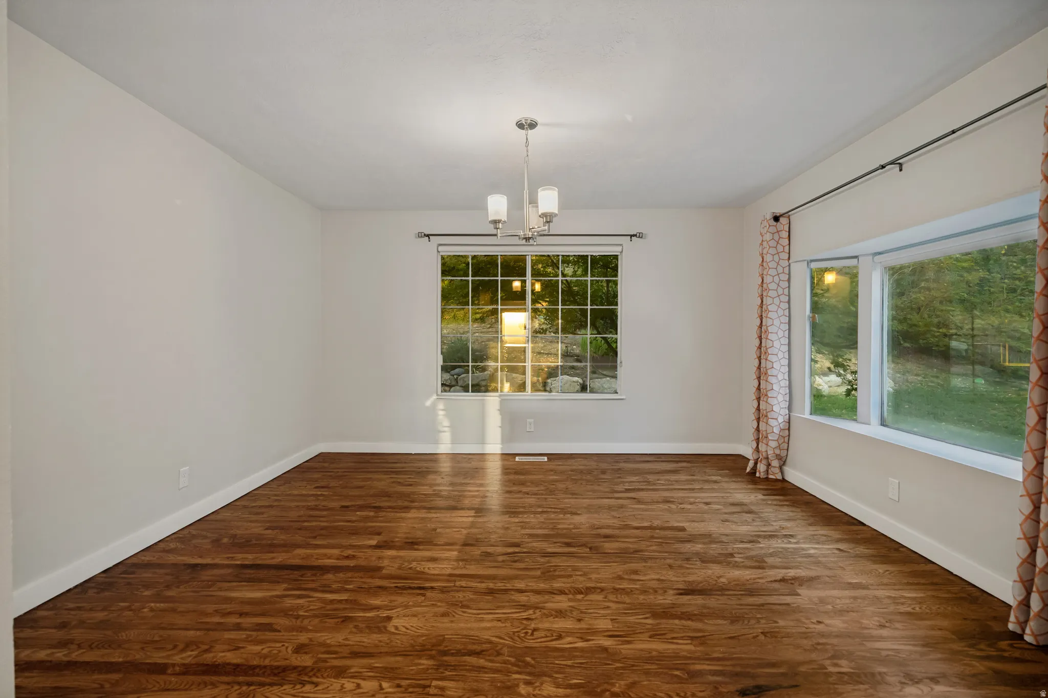 Hardwood flooring with a satin finish, neutral wall paint, and a multi-pane window with trim