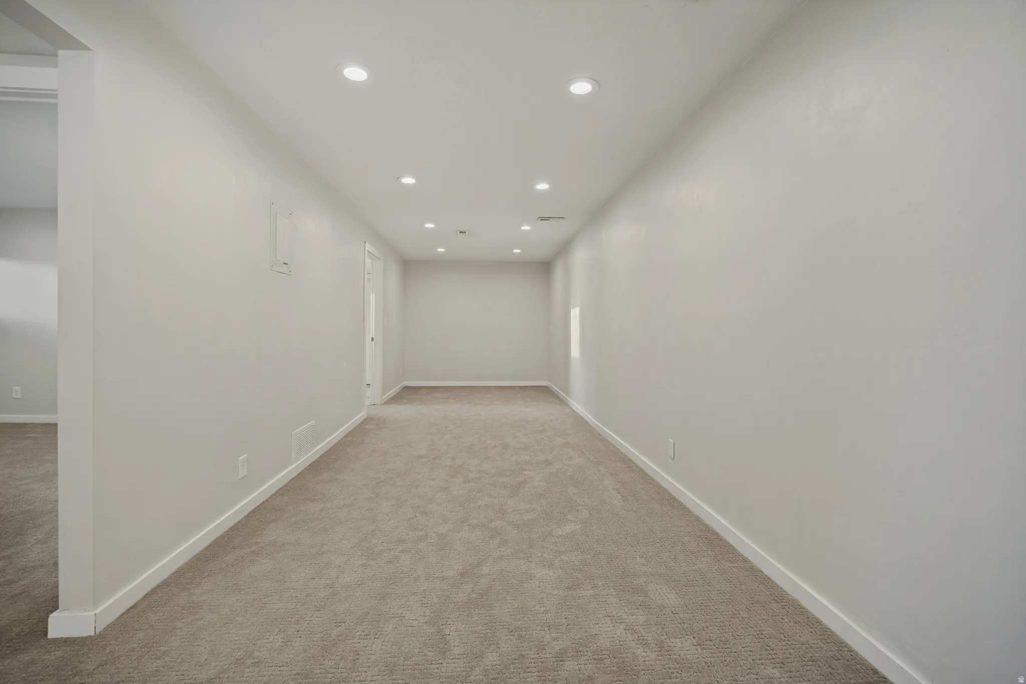 Recessed lighting illuminates the expansive room, featuring light gray carpeting and white trim