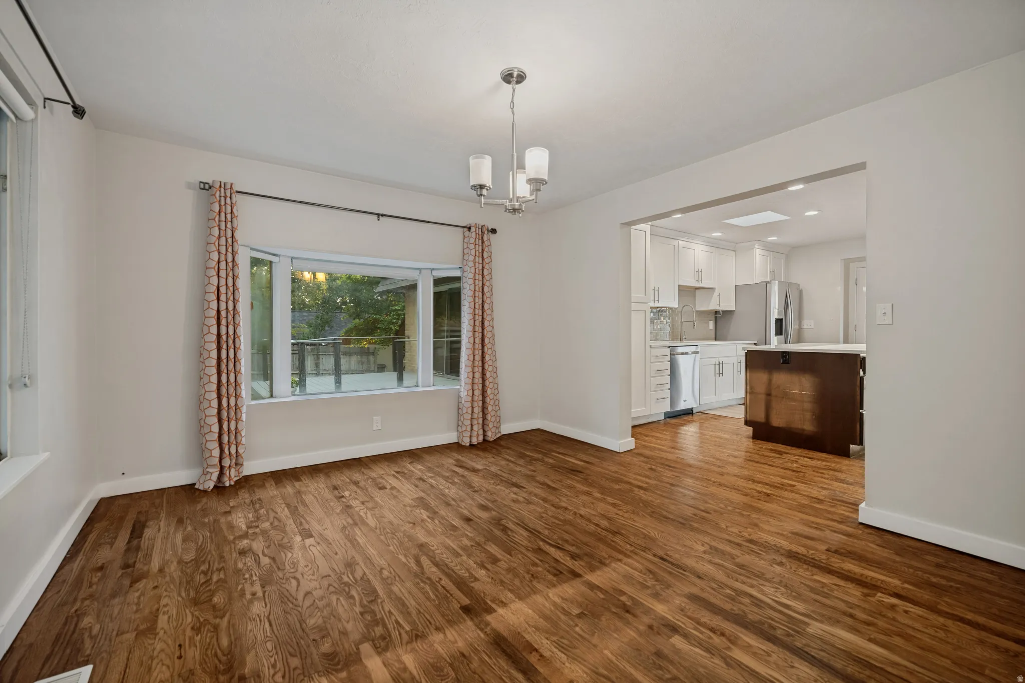 Hardwood flooring, bay window, recessed lighting, white cabinetry, and a kitchen island