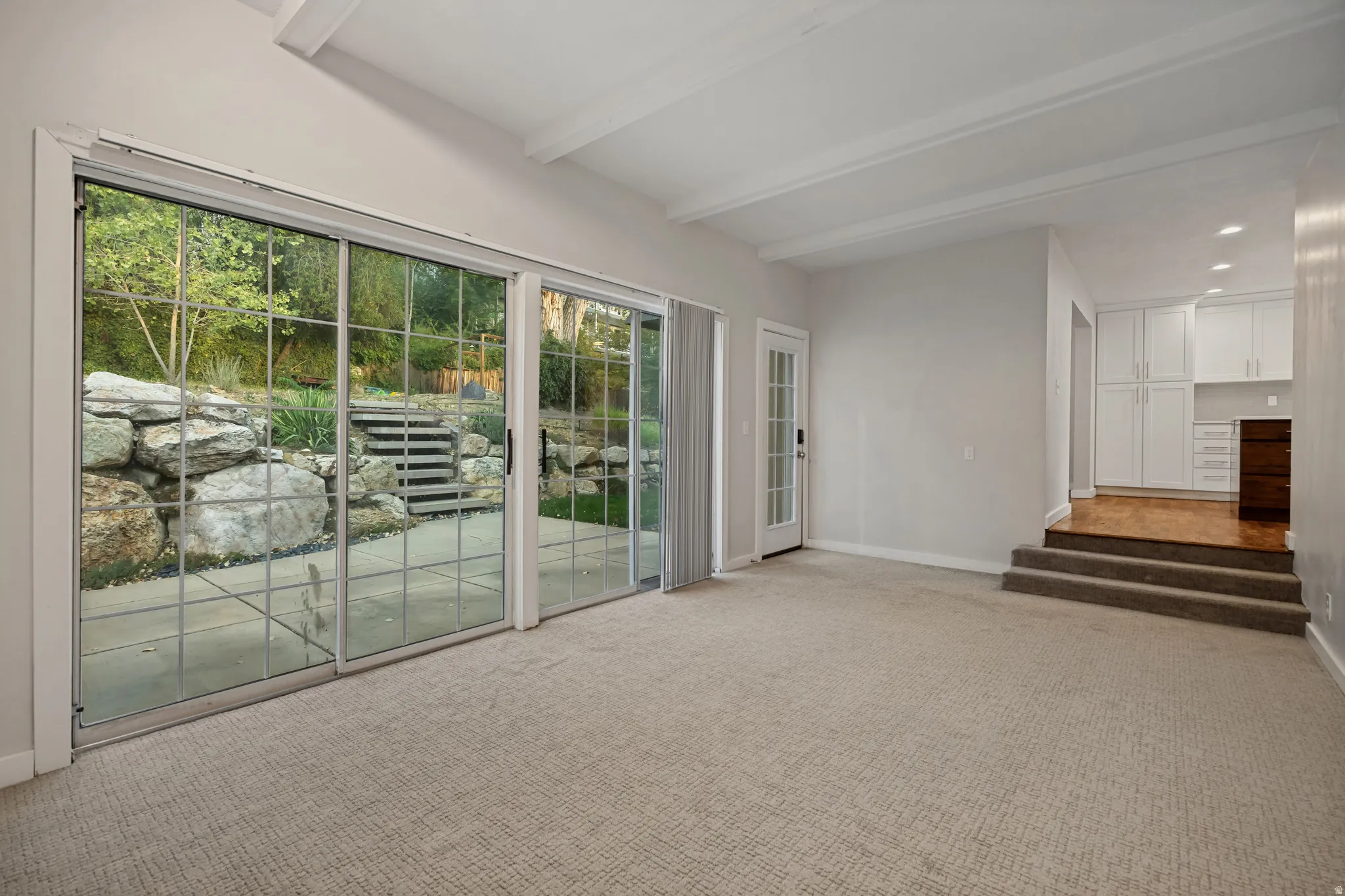 Expansive sliding glass doors, exposed beam ceiling, built-in white cabinetry, and a private stone patio with integrated steps