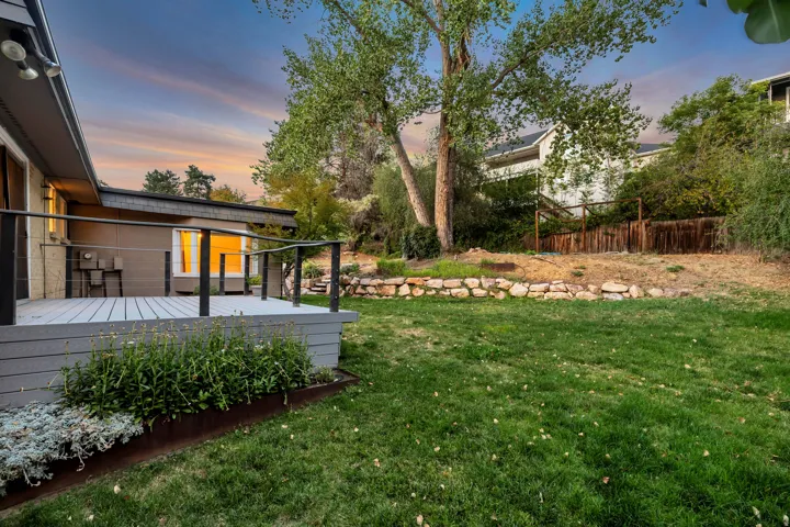 Expansive backyard featuring a large deck with cable railings, manicured lawn, and natural stone retaining walls