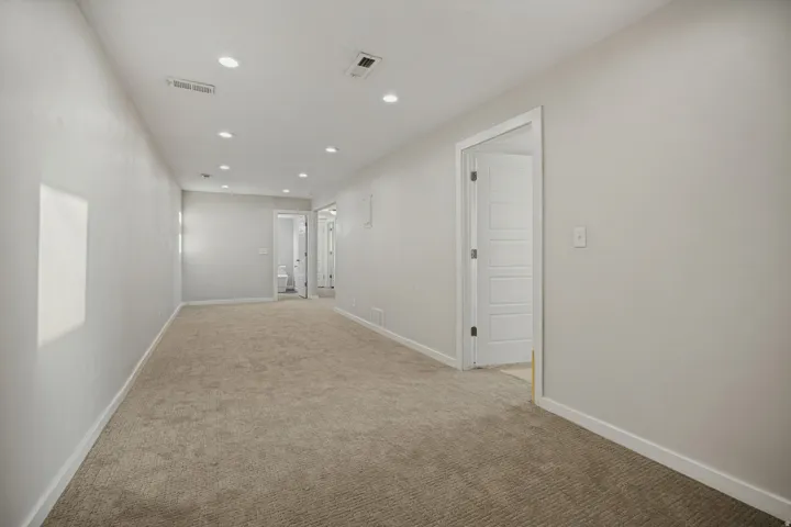 Recessed lighting, carpeted flooring, and a neutral wall color complement white trim and doors