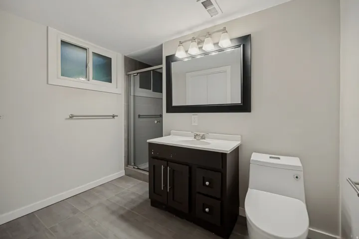 Bathroom featuring a dark wood-finish vanity, white countertop, framed mirror, and a glass-enclosed shower