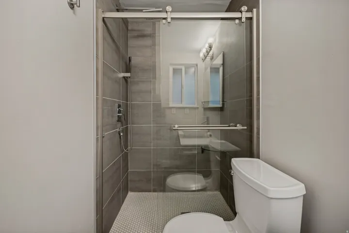 Walk-in shower with sliding glass door, large format tile surround, and mosaic tile flooring