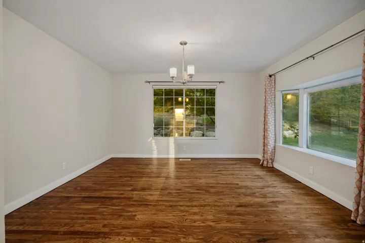 Hardwood flooring with a satin finish, neutral wall paint, and a multi-pane window with trim