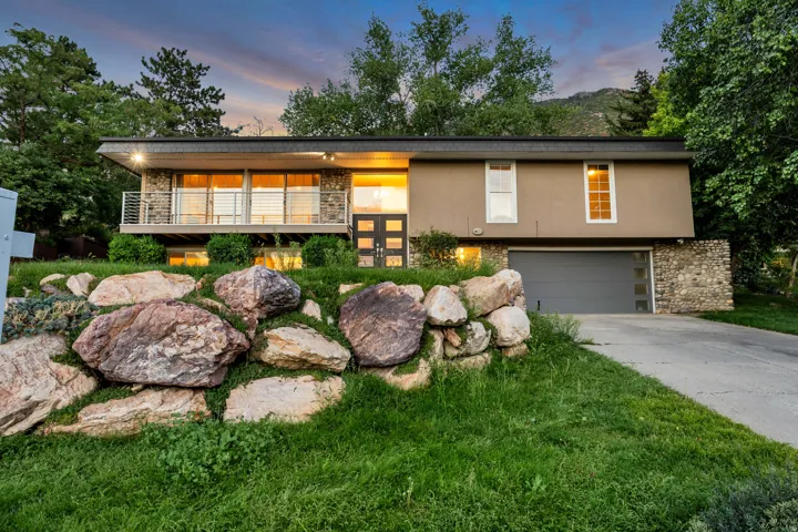 Modern exterior architecture with stone accents, a full-width balcony with cable railing, and an integrated garage