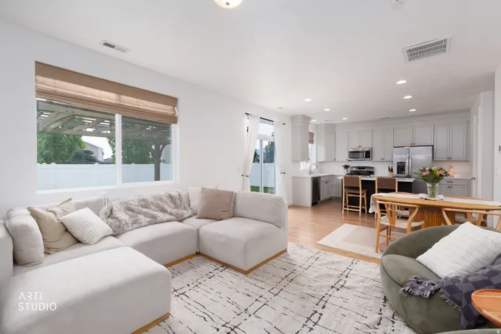 Open-concept living space with light wood-finish flooring, recessed lighting, and a white kitchen featuring shaker-style cabinetry, stainless steel appliances, and a dining area