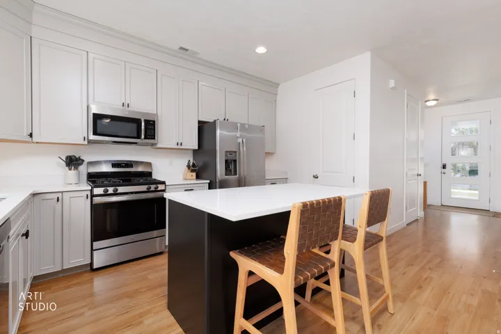 Modern kitchen featuring white shaker cabinetry, stainless steel appliances, a center island with a white countertop, and wood-finish flooring