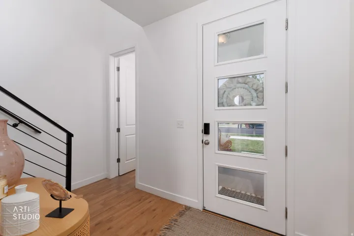 White entry door with multiple rectangular glass inserts, wood-finish flooring, and a modern black metal staircase railing