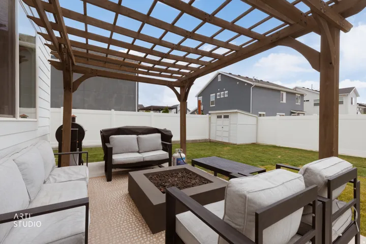 Pergola-covered patio featuring a built-in fire pit, privacy fencing, and a manicured lawn