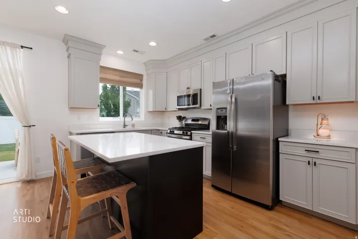 Kitchen featuring light cabinetry, a dark central island with a light countertop, stainless steel appliances, wood-finish flooring, and recessed lighting