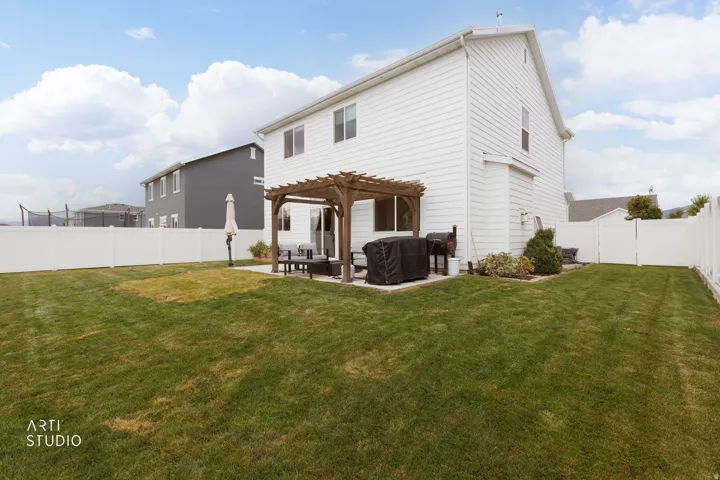 Expansive backyard featuring a manicured lawn, a concrete patio, a wooden pergola, and white privacy fencing