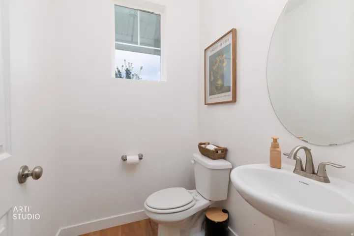 Pedestal sink with a two-handle faucet, round mirror, and a wall-mounted toilet paper holder