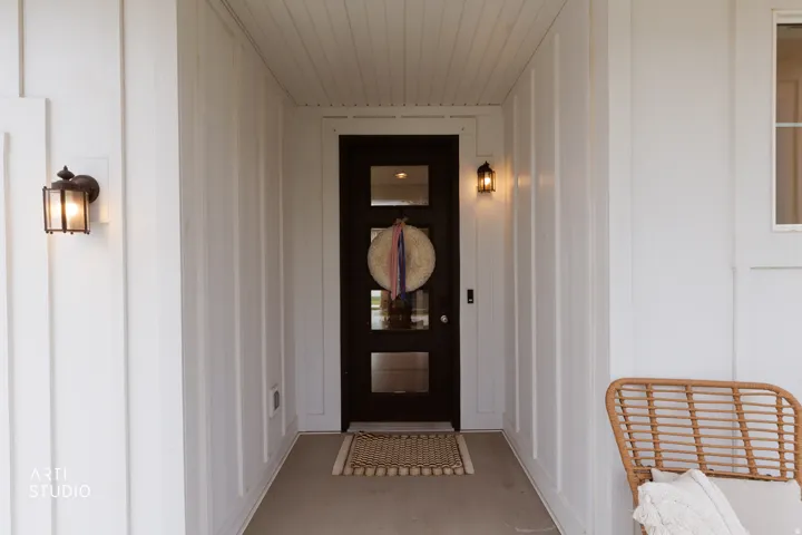 Recessed entry featuring board and batten siding, black entry door with frosted glass panels, and two matching bronze exterior light fixtures