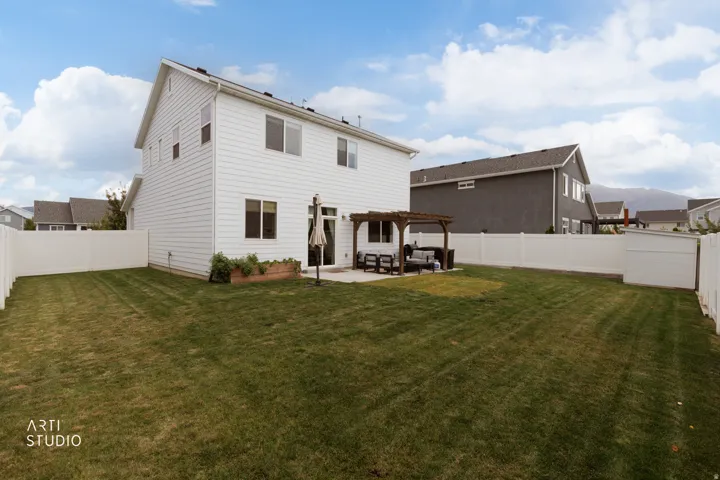Expansive backyard featuring a manicured lawn, full white vinyl fencing, a concrete patio, and a wood pergola