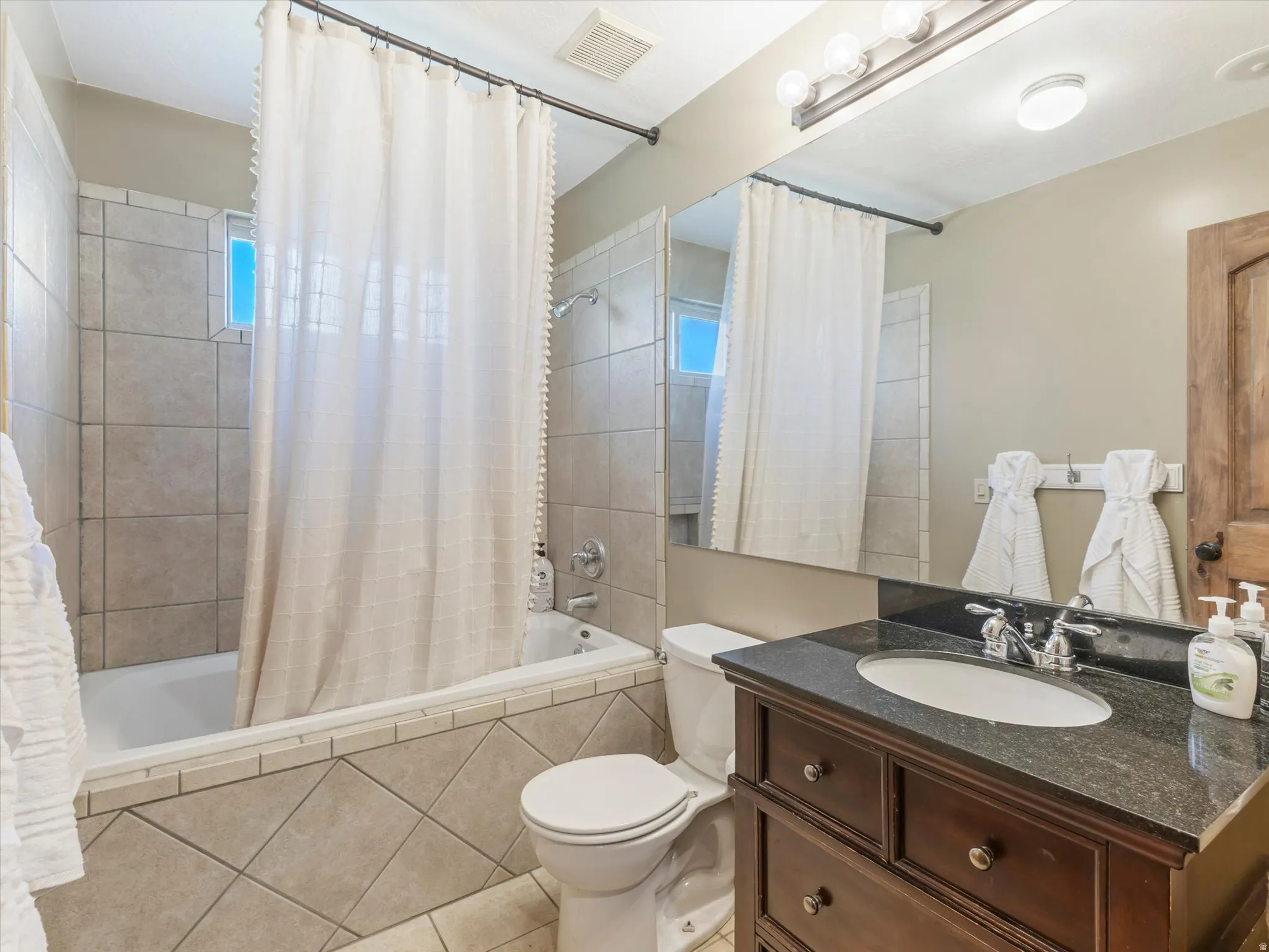 Spa-inspired bathroom featuring dual vanities with dark stone countertops, an undermount circular sink, polished nickel fixtures, and abundant recessed lighting