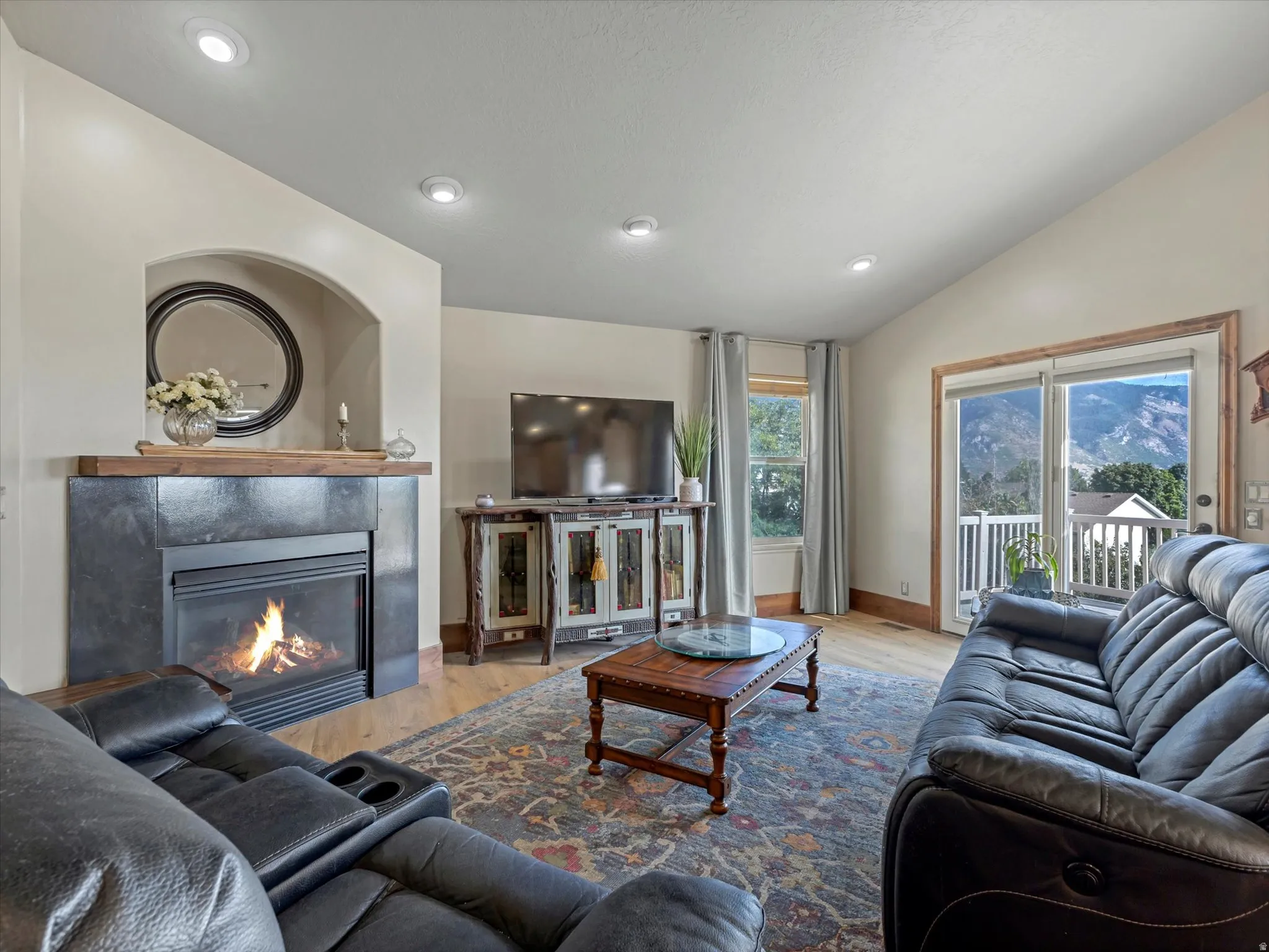 Fireplace with a wood mantle, vaulted ceiling, recessed lighting, wood-finish flooring, and sliding glass doors