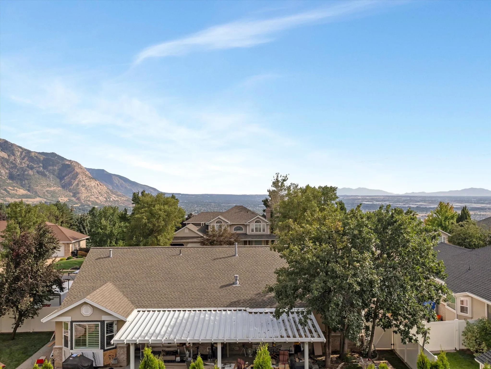 Expansive aerial perspective showcasing multiple residences with pitched roofs and composite shingle finishes, mature landscaping with established trees throughout the community, and distant mountain backdrop framing the residential setting