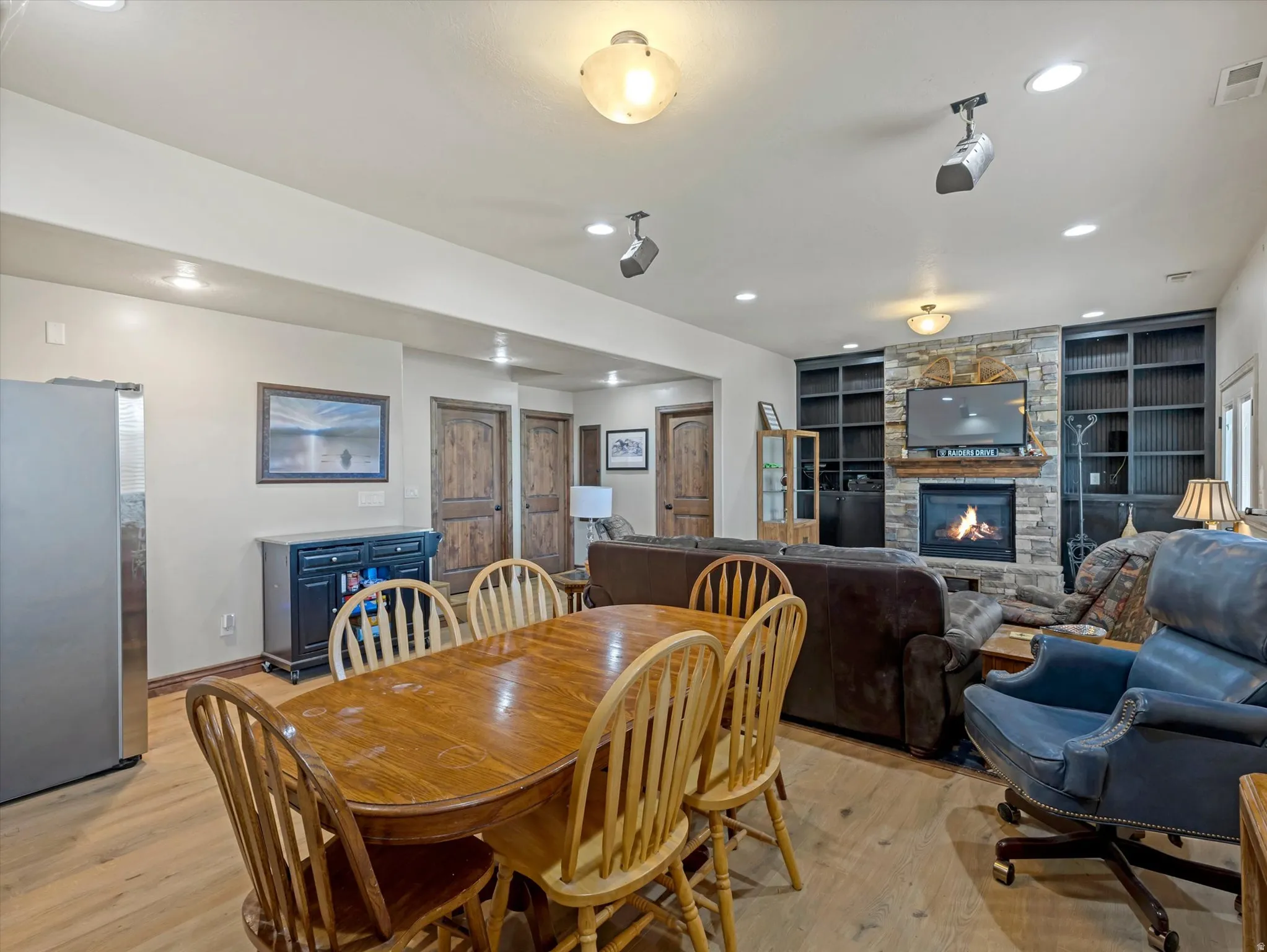Hardwood-finish flooring, recessed lighting, stone-front fireplace, built-in shelving, and wood-paneled doors