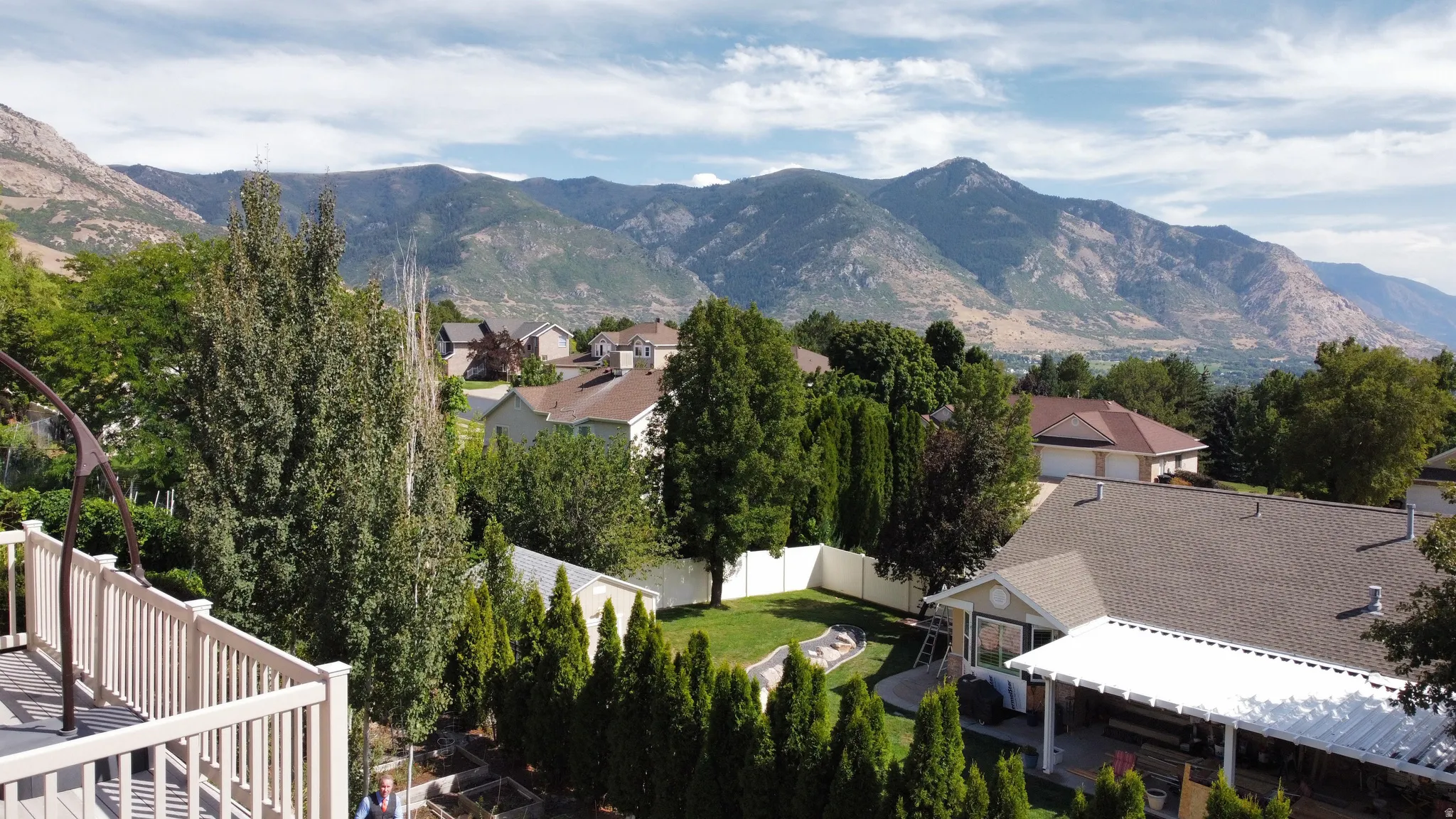 Elevated deck with railing, mountain backdrop, mature landscaping, and a covered patio area