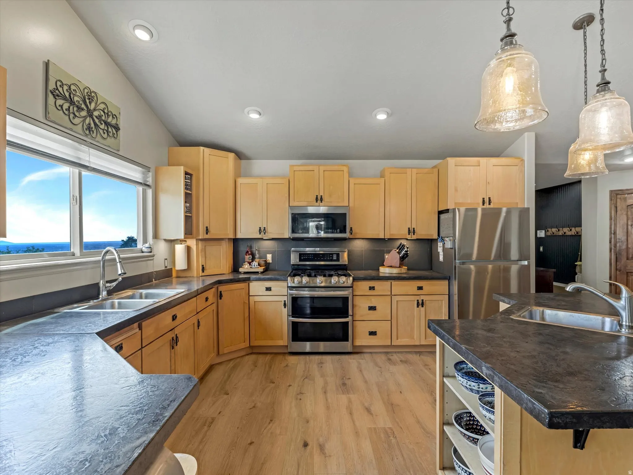 Chef's kitchen featuring natural wood cabinetry, stainless steel appliances including dual ovens, quartz countertops, pendant lighting, and abundant counter and storage space
