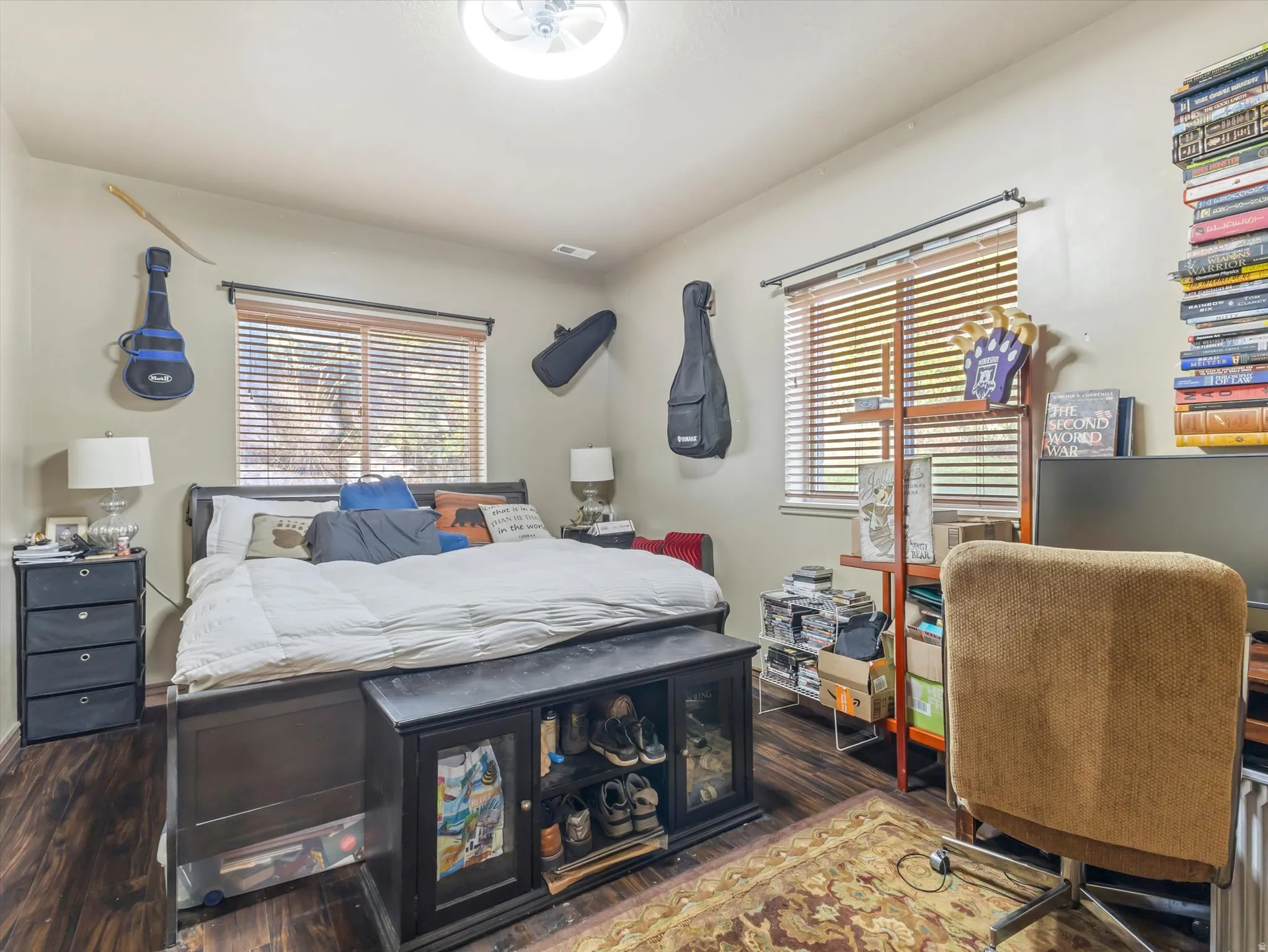 Basement Bedroom 1 - Bright secondary bedroom featuring wood-finish flooring, multiple windows with plantation shutters, built-in shelving with display space, and dark wood bed frame with integrated storage drawers