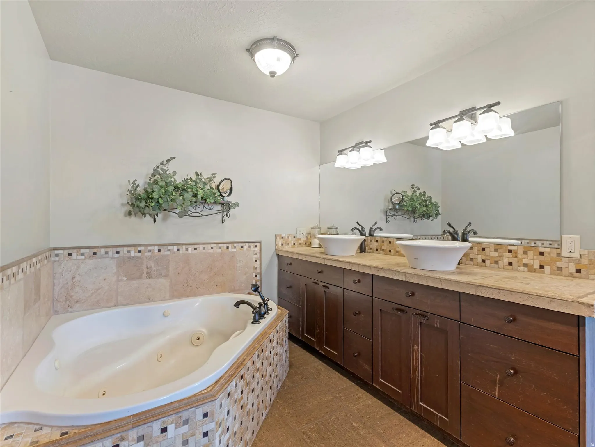 Master Bathroom - Corner jetted tub with tiled surround, dual vessel sinks, extensive vanity with dark wood-finish cabinetry, and a large mirror