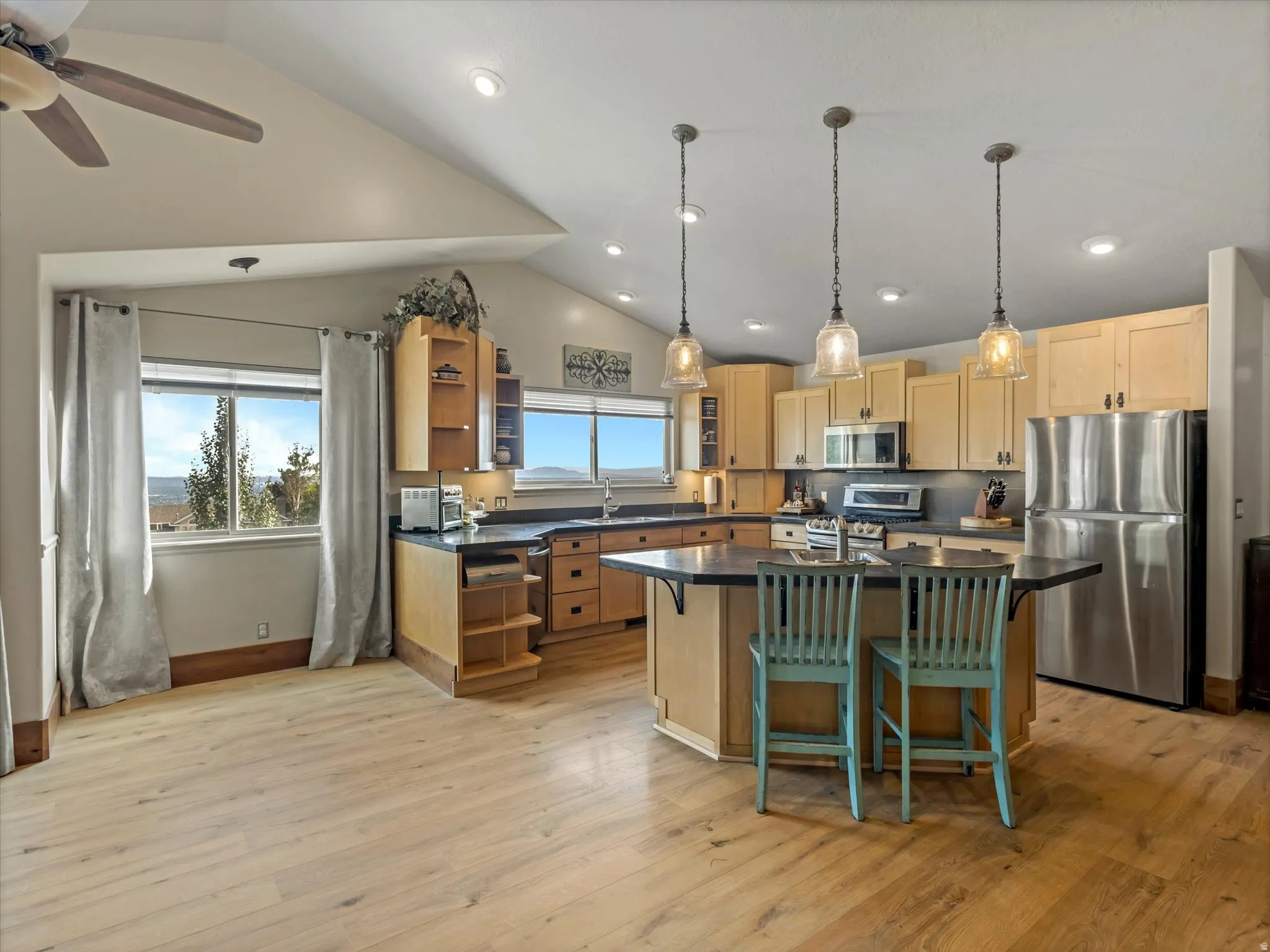 Vaulted ceiling with recessed lighting, wood-finish flooring, kitchen island with seating, stainless steel appliances, and wood cabinetry