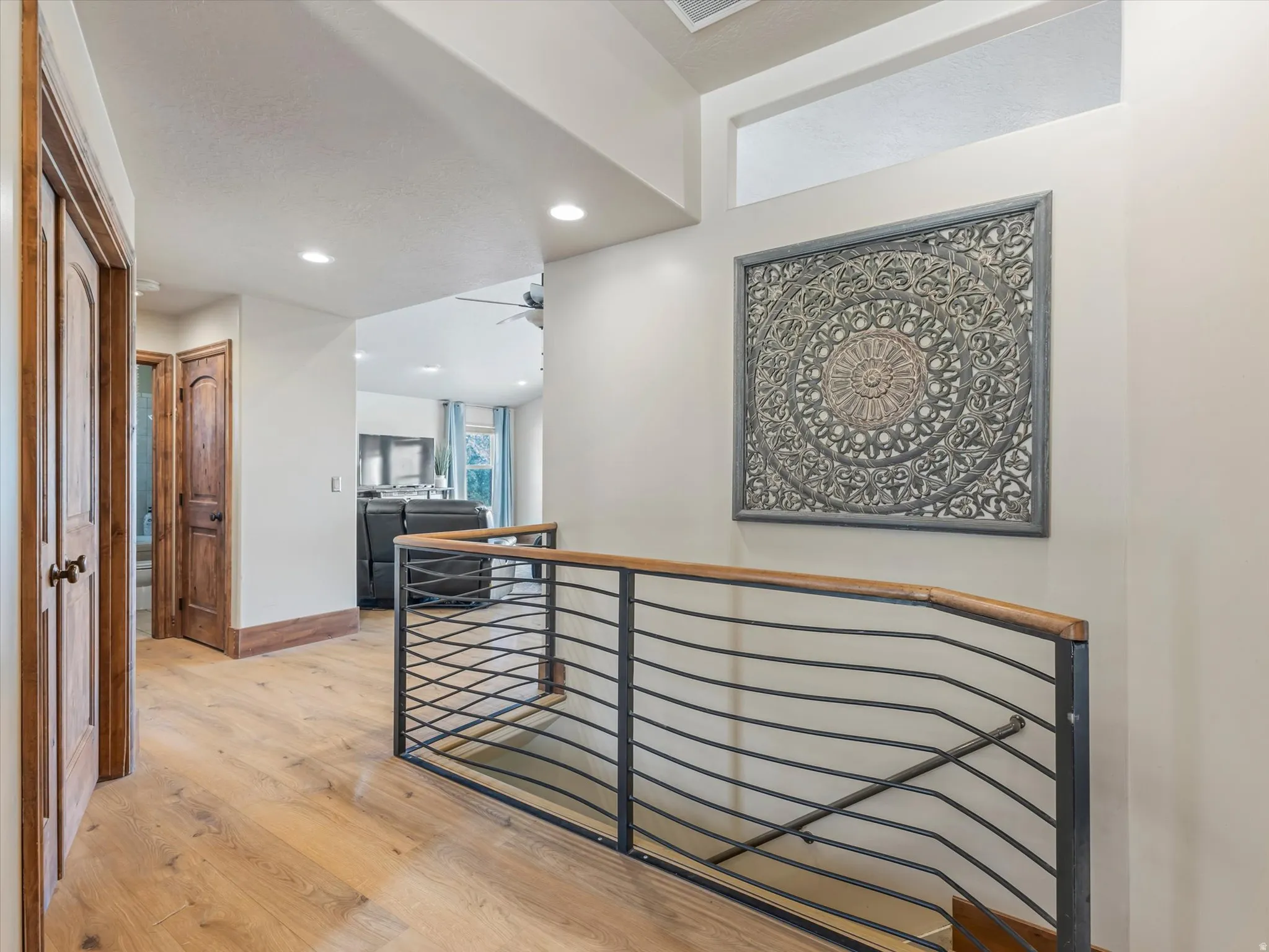 Stairs to basement - Modern hallway featuring gleaming wood-finish flooring, recessed ceiling lighting, and a contemporary metal railing with horizontal cable detailing