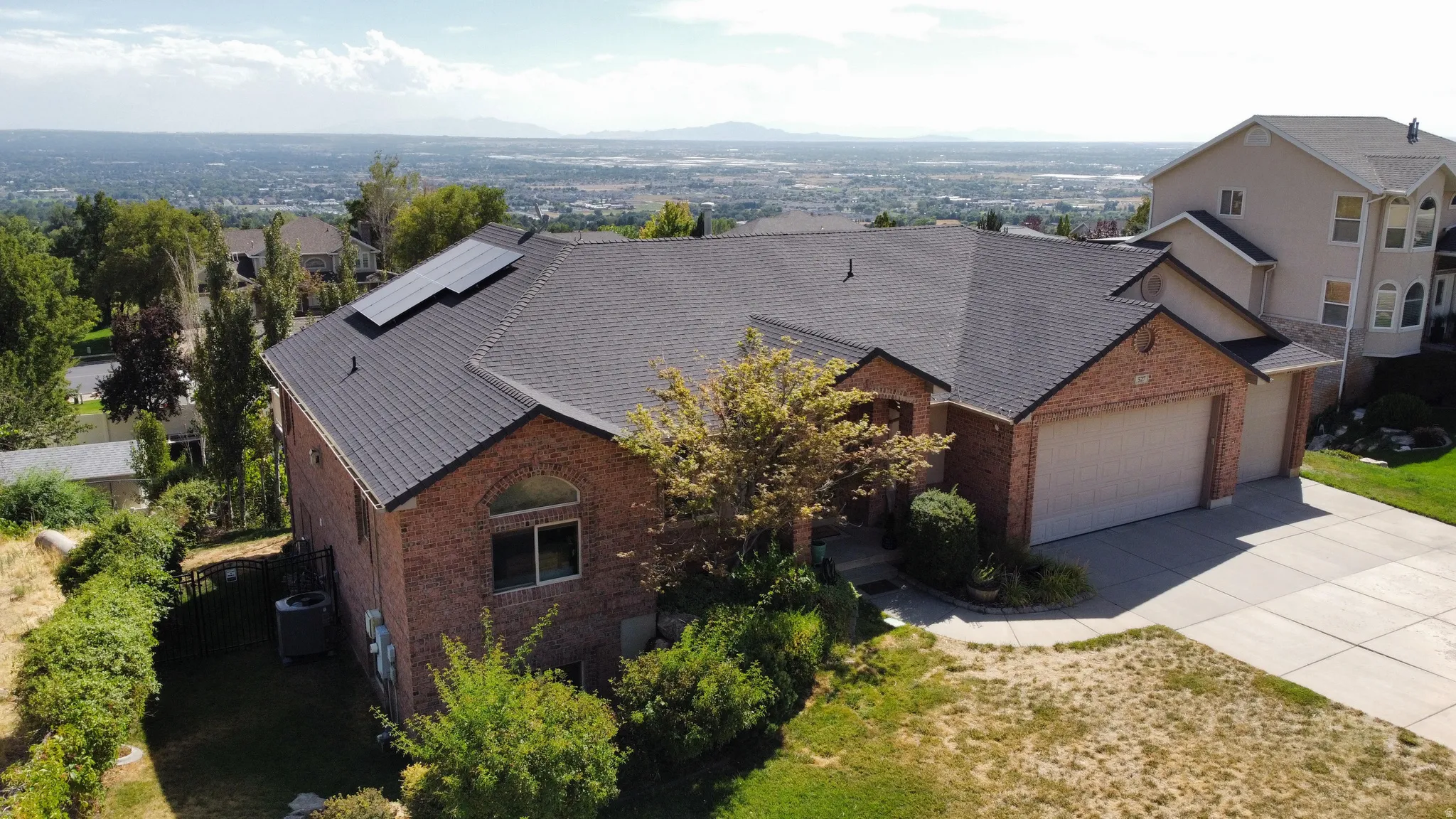 Brick exterior, multi-panel roof, attached two-car garage, solar panels, and concrete driveway