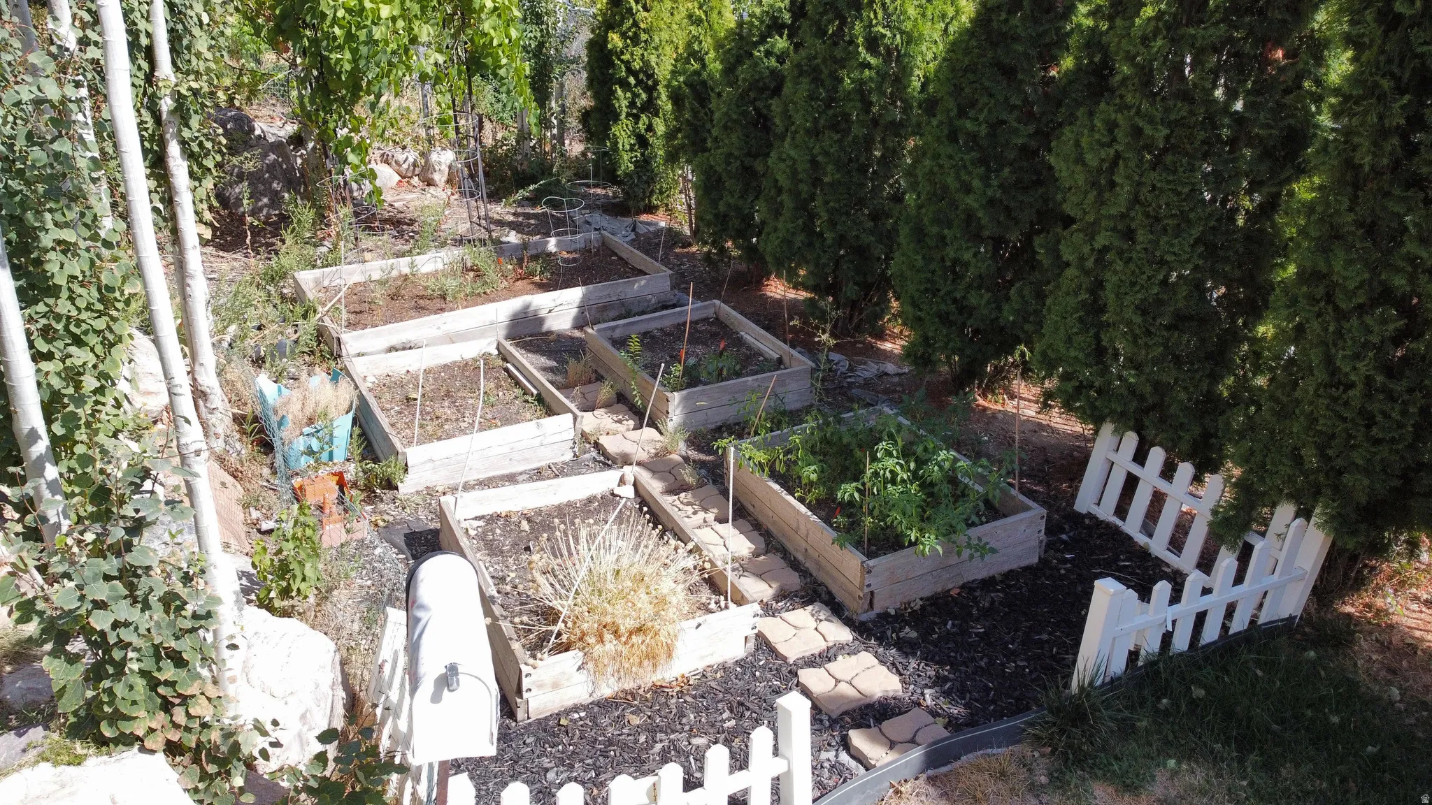 Terraced garden beds, stone paver pathway, decorative white picket fencing, and established perimeter plantings