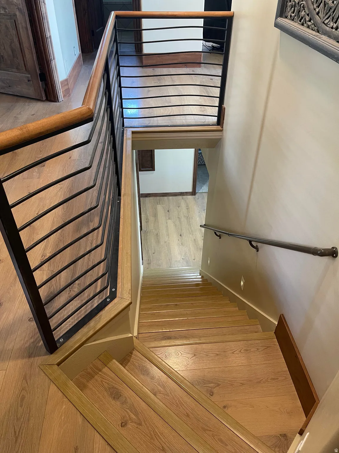 Stairwell featuring wood-finish flooring, metal and wood handrailing, and wall-mounted lighting