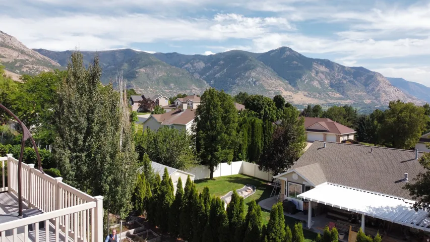 Elevated deck with railing, mountain backdrop, mature landscaping, and a covered patio area
