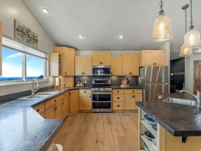 Chef's kitchen featuring natural wood cabinetry, stainless steel appliances including dual ovens, quartz countertops, pendant lighting, and abundant counter and storage space