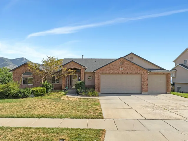 Brick Colonial home featuring a two-car garage, manicured front lawn with mature landscaping, concrete driveway, and mountain backdrop