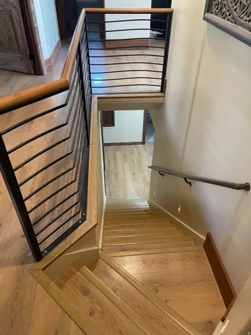 Stairwell featuring wood-finish flooring, metal and wood handrailing, and wall-mounted lighting
