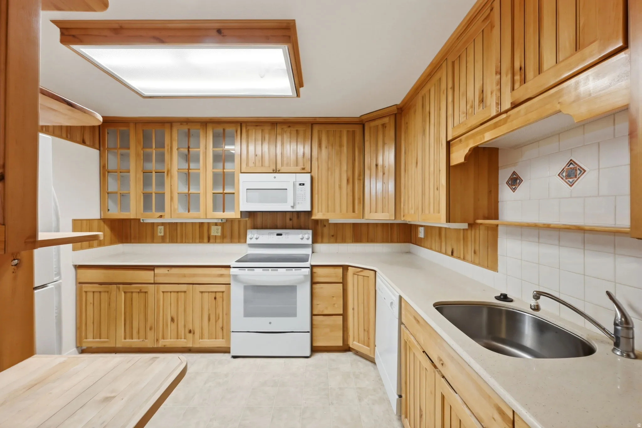 Kitchen featuring wood-paneled cabinetry, white countertops, built-in stainless steel sink, and white appliances