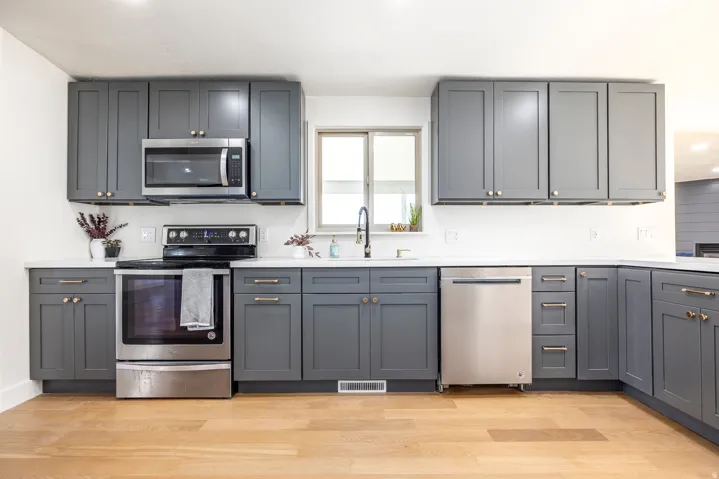 Modern kitchen featuring gray shaker-style cabinetry, stainless steel appliances, white countertops, and wood-finish flooring