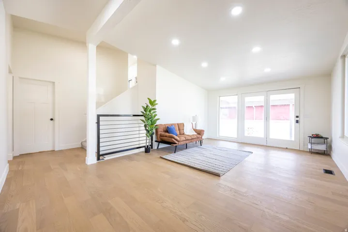 Spacious room featuring wood-finish flooring, recessed lighting, and a metal horizontal bar railing leading to an upper level