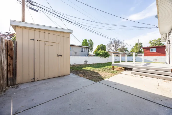 Concrete patio, elevated deck with railings, storage shed with single door, wood fence, and partial lawn area