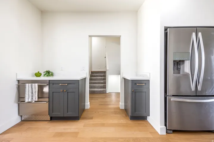 Stainless steel refrigerator, wood-finish flooring, white countertops, built-in stainless steel appliance, and dark gray cabinetry
