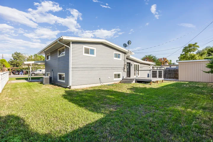Expansive lawn area, multi-level house with grey siding, white-railed deck, and a detached storage shed