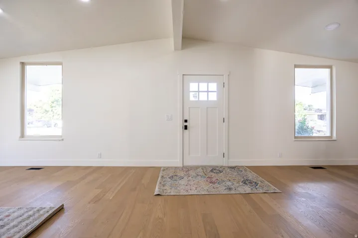 Vaulted ceilings, recessed lighting, wood-finish flooring, two large windows, and a panel door with multiple lites
