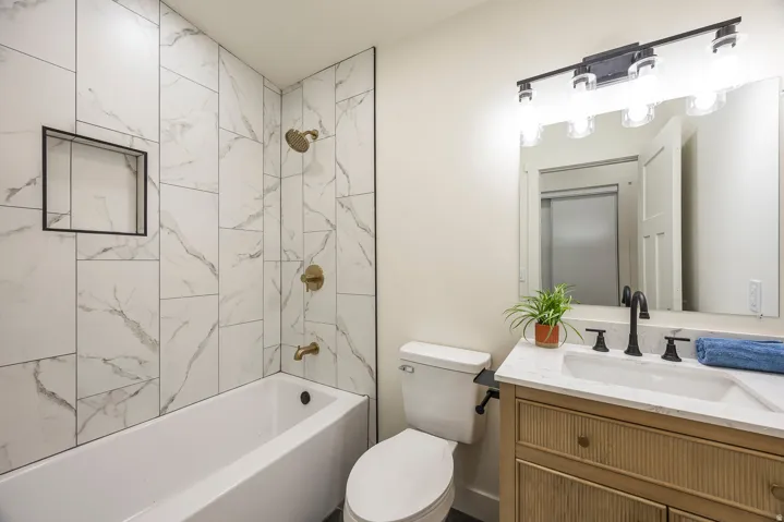 Bathroom featuring a white bathtub, floor-to-ceiling tiled shower surround, recessed shower niche, and a vanity with an integrated sink and matte black faucet