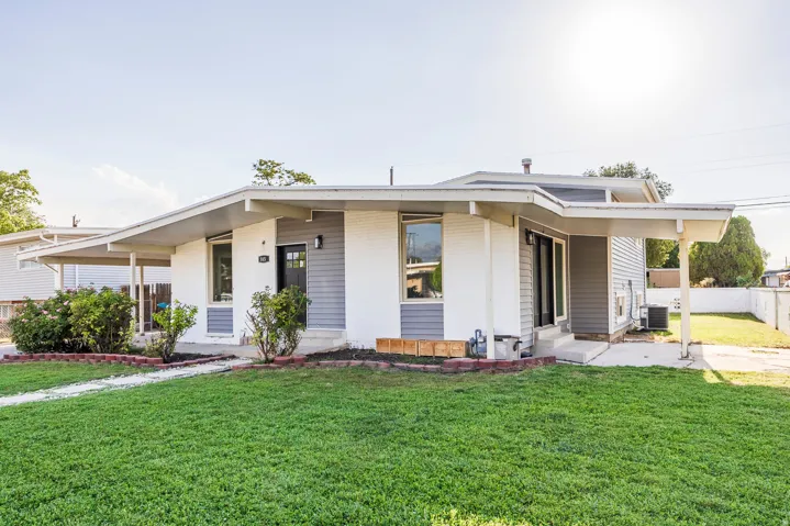 Exterior featuring white brick and gray siding, front walkway, established landscaping, and an attached carport